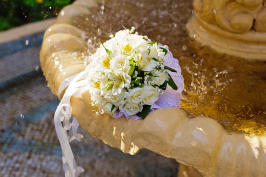 The Wedding Bouquet Of The Bride Of Red Roses Lies In An Old Fountain Under Splashes And Drops Of Water.. bridal bouquet of flowers in fountain water drops