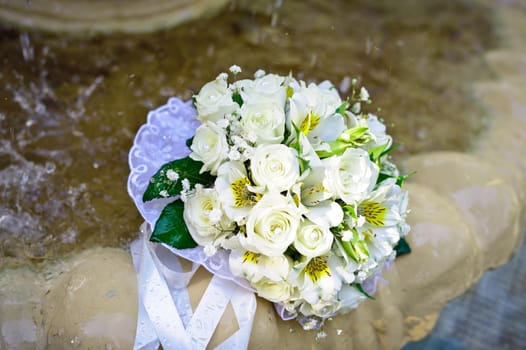 The Wedding Bouquet Of The Bride Of Red Roses Lies In An Old Fountain Under Splashes And Drops Of Water.. bridal bouquet of flowers in fountain water drops