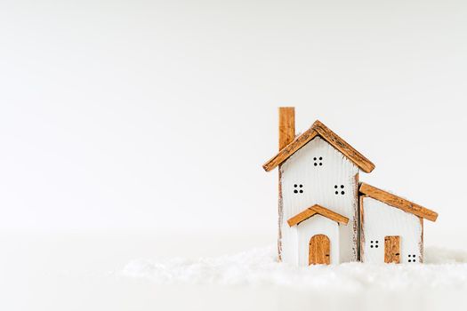 Happy New Year and Merry Christmas banner. Festive white background with toy wooden house, snow, rustic Christmas village and decoration. Copy space for winter holidays greeting card.