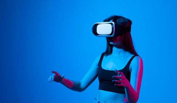 Inspired brunette happy woman getting experience using VR-headset glasses of virtual reality much gesticulating hands in neon light