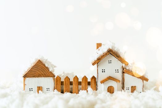 Happy New Year and Merry Christmas postcard. Festive white background with toy wooden house, snow, light bokeh, christmas village and decoration. Copy space for winter holidays greeting card.