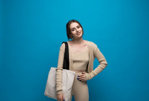 Beautiful brunette woman in a beige costume with cotton bag on a shoulder on a grey background. Mockup and zero waste concept