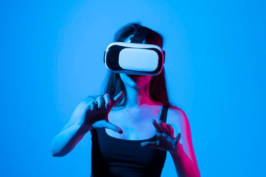 Young brunette woman in black t-shirt wearing a VR headset and looking up while playing a game with a friends in a metaverse. Virtual reality concept