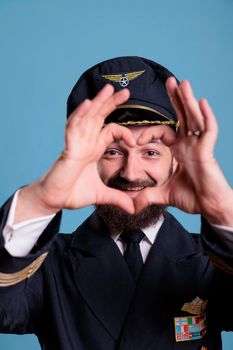 Smiling airliner pilot showing heart shaped love symbol with fingers, conceptual romance gesture. Friendly airplane aviator in uniform expressing affection feelings front view medium shot