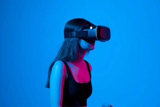 Confident brunette young woman in virtual reality headset pointing in the air while standing in a studio space. Using VR technologies