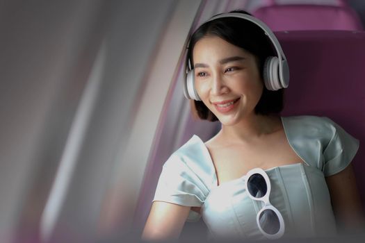 portrait of A successful asian business woman in a plane sits in a business class seat and uses a Around-Ears Headphones for playing music during flight. relax concept.