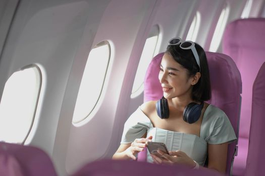 Young woman sitting with phone on the aircraft seat near the window during the flight in the airplane.