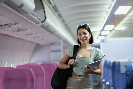 Portrait of a woman holding a shoulder bag and holding a tablet while standing on a passenger plane.