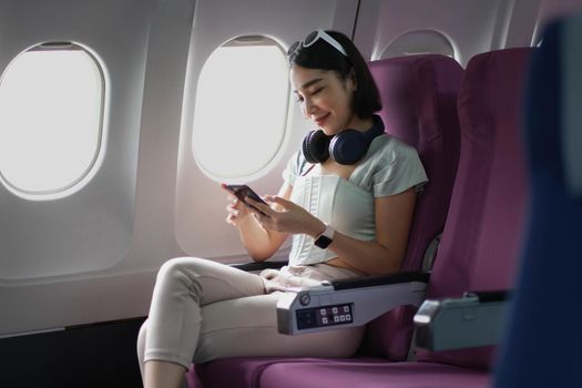 Young woman sitting with phone on the aircraft seat near the window during the flight in the airplane.