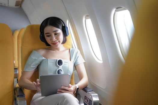 Travel tourism with modern technology and air flights concept, woman sitting in plane with modern digital gadget and searching favourite music playlist in application for listening.