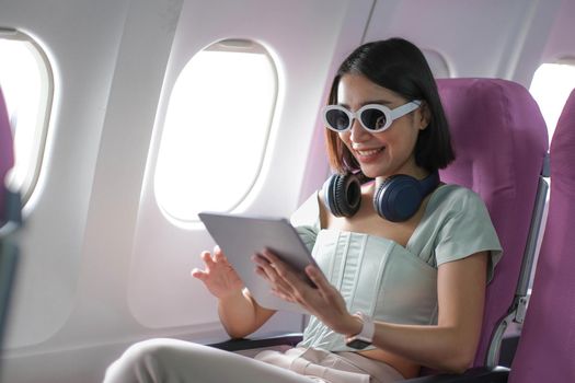 Travel tourism with modern technology and air flights concept, woman sitting in plane with modern digital gadget and searching favourite music playlist in application for listening.