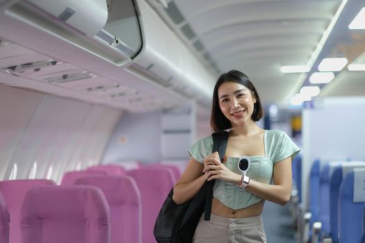 portrait of a woman carries a suitcase over her shoulder while standing in a passenger on a plane