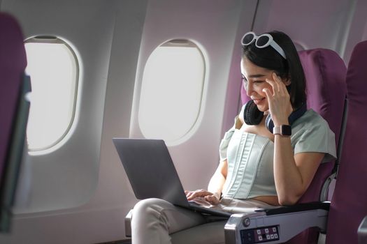 Asian young woman using laptop sitting near windows at first class on airplane during flight,Traveling and Business concept.