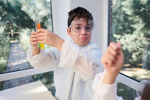 Caucasian curious smart child, a schoolboy looking at the camera while making chemical experiments in chemistry laboratory. Chemistry education. Back to school on new semester of new academic year