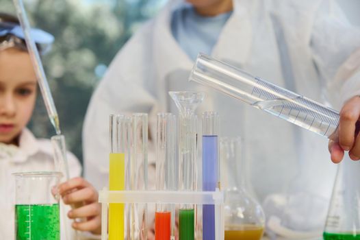Selective focus on measuring cylinder in the hands of school child, pouring water into test tubes with colorful chemical liquids, during chemistry lesson. Back to school in new academic year semester