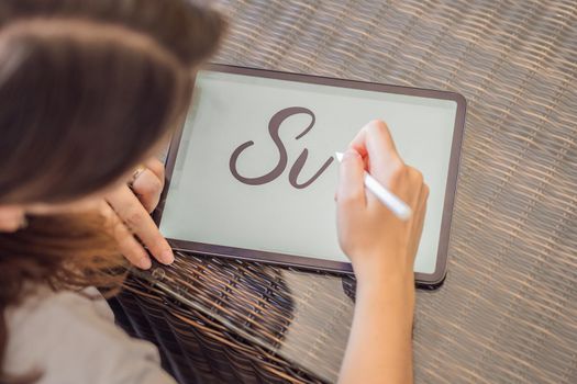 Calligrapher Young Woman writes phrase on digital tablet. Inscribing ornamental decorated letters. Calligraphy, graphic design, lettering, handwriting, creation.