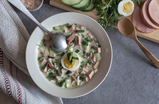 Traditional Russian cold summer soup - okroshka with fresh vegetables, sausage and kefir. Composition with traditional dishes and spices. View from above.