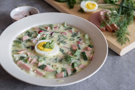 Traditional Russian cold summer soup - okroshka with fresh vegetables, sausage and kefir. Composition with traditional dishes and spices. View from above.