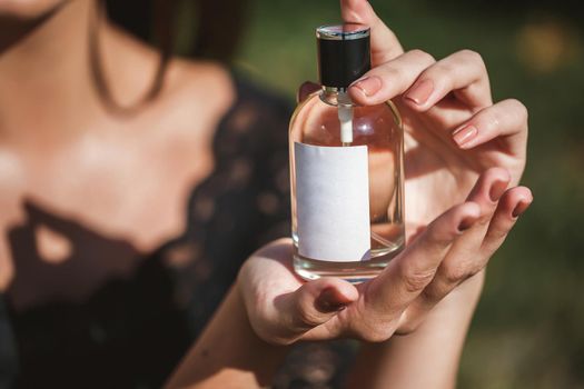 Perfume bottle of a female hand. Young stylish woman holding a bottle of perfume. Fashionable perfume in the hands of women. Girl spraying perfume. Beautiful female hands. Perfumes for women