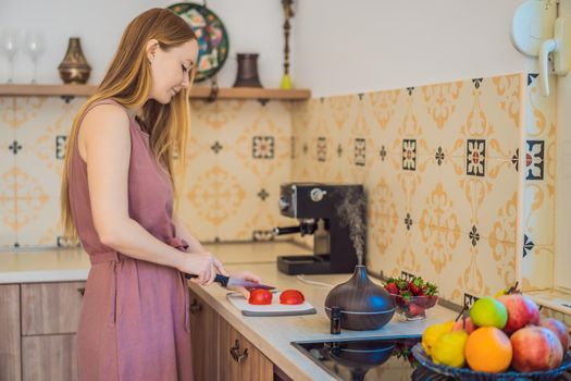 Woman prepares food next to an aroma diffuser. cook cuts ripe red peppers in the kitchen. Cooking fresh, ripe, bell pepper salad for guests. Summer fresh vegetable salad.