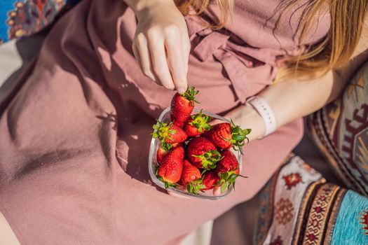Portrait of gorgeous woman wearing beautiful dress sitting in a patio and eating strawberry.