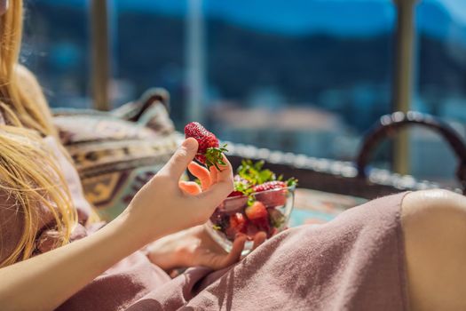 Portrait of gorgeous woman wearing beautiful dress sitting in a patio and eating strawberry.