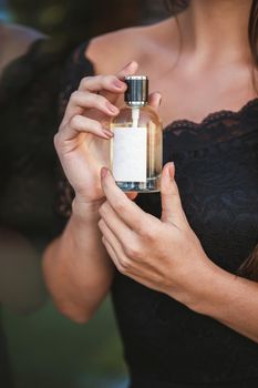 Perfume bottle of a female hand. Young stylish woman holding a bottle of perfume. Fashionable perfume in the hands of women. Girl spraying perfume. Beautiful female hands. Perfumes for women