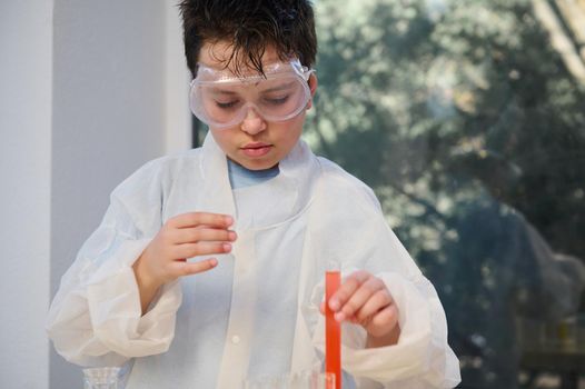 Handsome Caucasian ten years old schoolboy, experimenting with chemicals and liquid solutions, during a chemistry class. Smart child boy fascinated by learning Chemistry. Magical chemical reactions