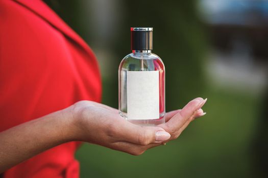 Perfume bottle of a female hand. Young stylish woman holding a bottle of perfume. Fashionable perfume in the hands of women. Girl spraying perfume. Beautiful female hands. Perfumes for women