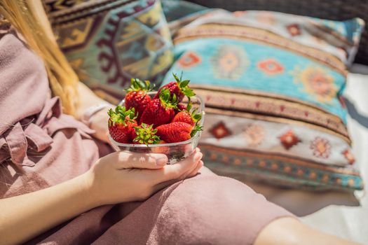 Portrait of gorgeous woman wearing beautiful dress sitting in a patio and eating strawberry.