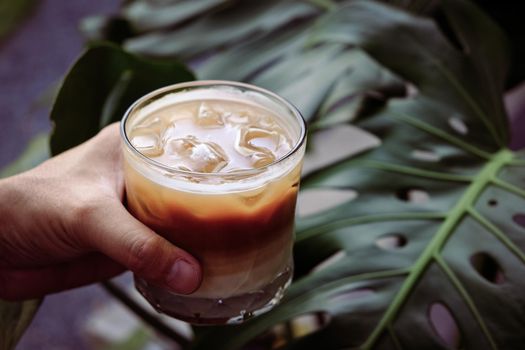 Hand hold iced latte coffee in a  tall glass. cold summer drink  with green nature background