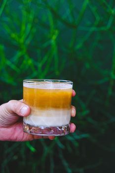 Hand hold iced latte coffee in a  tall glass. cold summer drink  with green nature background