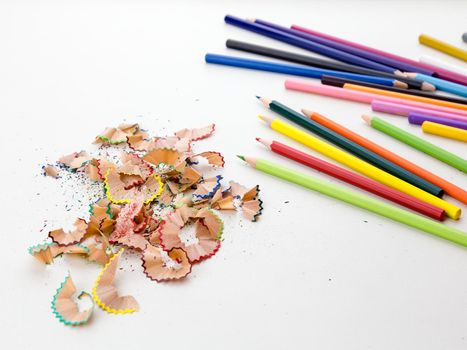 Colored pencil crayons in a row with shavings on white background