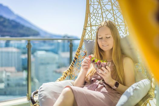 Portrait of gorgeous woman wearing beautiful dress sitting in a patio and eating strawberry.