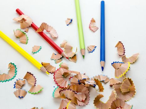 Colored pencil crayons in a row with shavings on white background