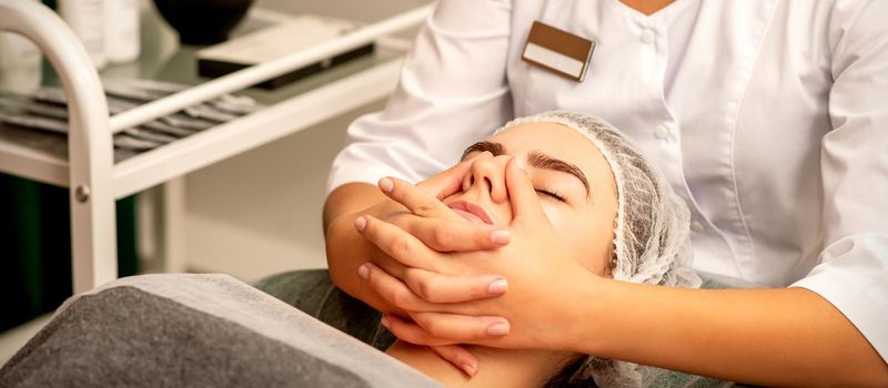 Beautiful young caucasian woman with closed eyes receiving a facial massage in a beauty salon