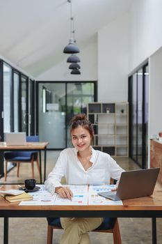 Portrait of a beautiful female employee holding a pen, using a computer and checking the company's budget documents