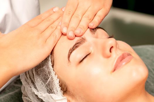 Head massage. Beautiful caucasian young white woman receiving a head and forehead massage with closed eyes in a spa salon