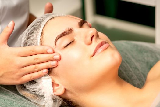 Head massage. Beautiful caucasian young white woman receiving a head and forehead massage with closed eyes in a spa salon