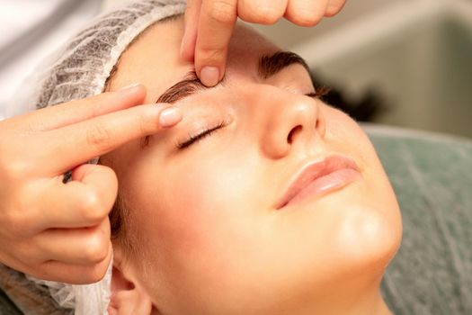 Eyebrow massage. Beautiful caucasian young white woman receiving an eye and eyebrow massage with closed eyes in a spa salon