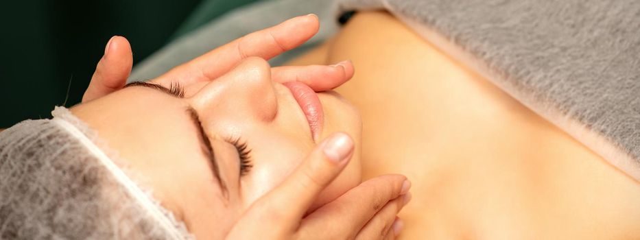 Beautiful young caucasian woman with closed eyes receiving a facial massage in a beauty salon