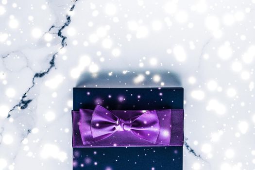 Branding, glamour and cold season concept - Winter holiday gift box with purple silk bow, snow glitter on marble background as Christmas and New Years presents for luxury beauty brand, flatlay design