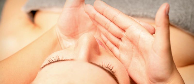 Beautiful caucasian young woman receiving a facial massage with closed eyes in spa salon, close up. Relaxing treatment concept