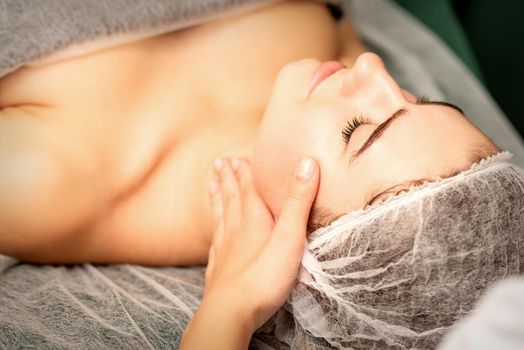 Facial massage. Hands of a masseur massaging neck of a young caucasian woman in a spa salon, the concept of health massage