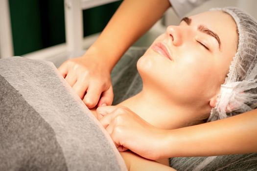 Massaging female breast, and shoulder. Young beautiful caucasian woman with closed eyes receiving chest and shoulders massage in beauty spa salon