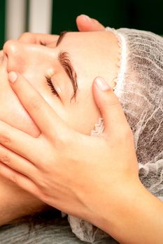 Beautiful young caucasian woman with closed eyes receiving a facial massage in a beauty salon