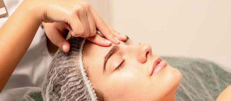 Beautiful caucasian young woman receiving a facial massage with closed eyes in spa salon, close up. Relaxing treatment concept