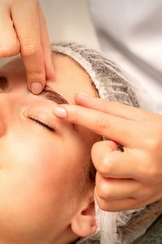 Eyebrow massage. Beautiful caucasian young white woman receiving an eye and eyebrow massage with closed eyes in a spa salon