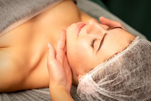 Facial massage. Hands of a masseur massaging neck of a young caucasian woman in a spa salon, the concept of health massage