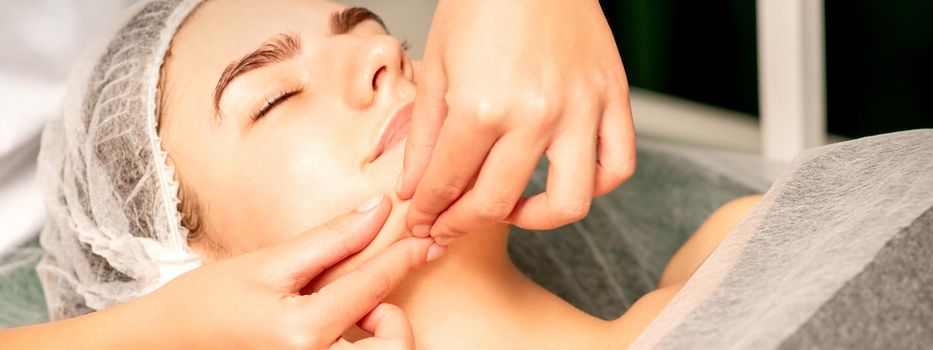 Beautiful young caucasian woman with closed eyes receiving a facial massage in a beauty salon